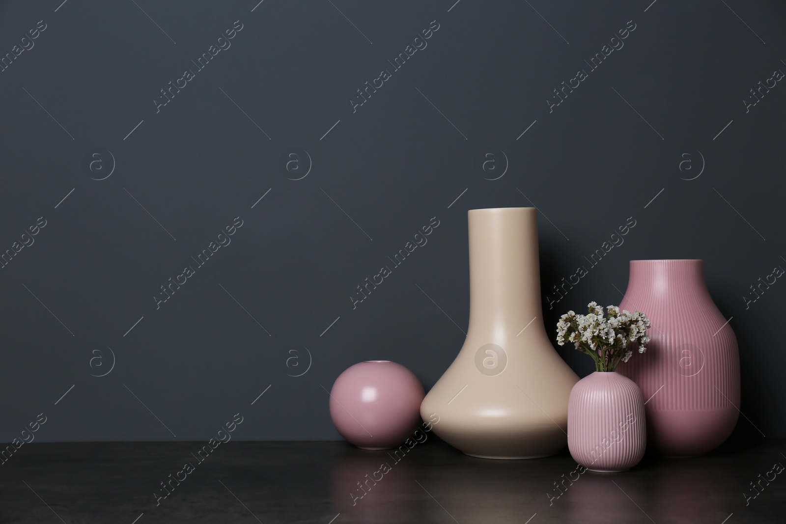 Photo of Beautiful ceramic vases and flowers on table against color wall with space for text