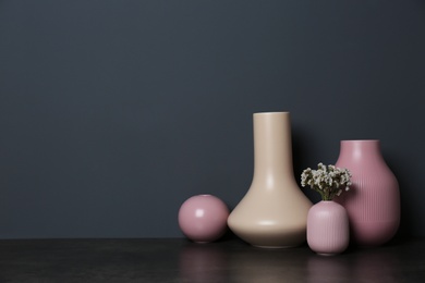 Photo of Beautiful ceramic vases and flowers on table against color wall with space for text