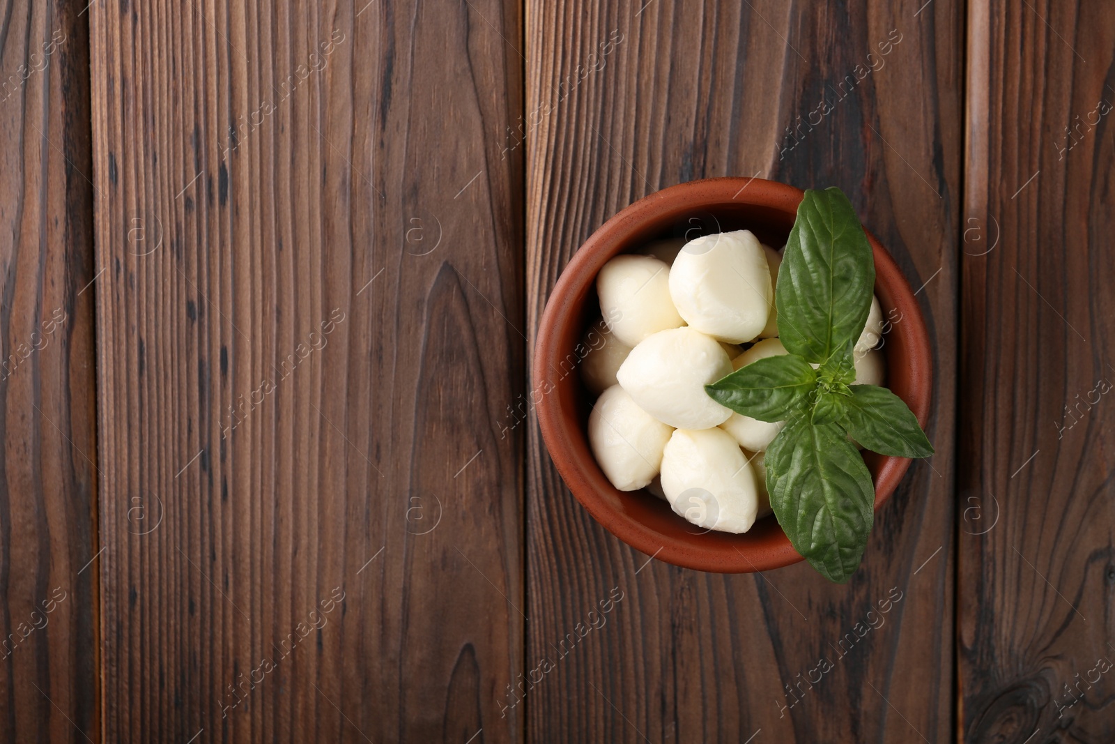 Photo of Tasty mozarella balls and basil leaves in bowl on wooden table, top view. Space for text