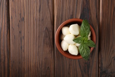Photo of Tasty mozarella balls and basil leaves in bowl on wooden table, top view. Space for text