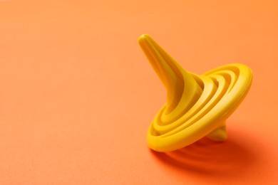 Photo of One yellow spinning top on orange background, closeup. Space for text
