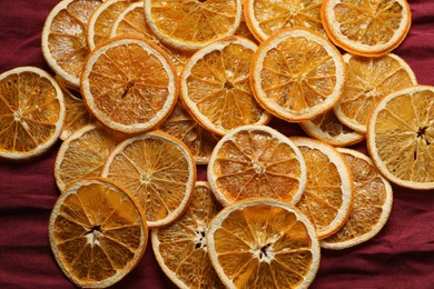 Photo of Heap of dry orange slices on burgundy fabric, flat lay