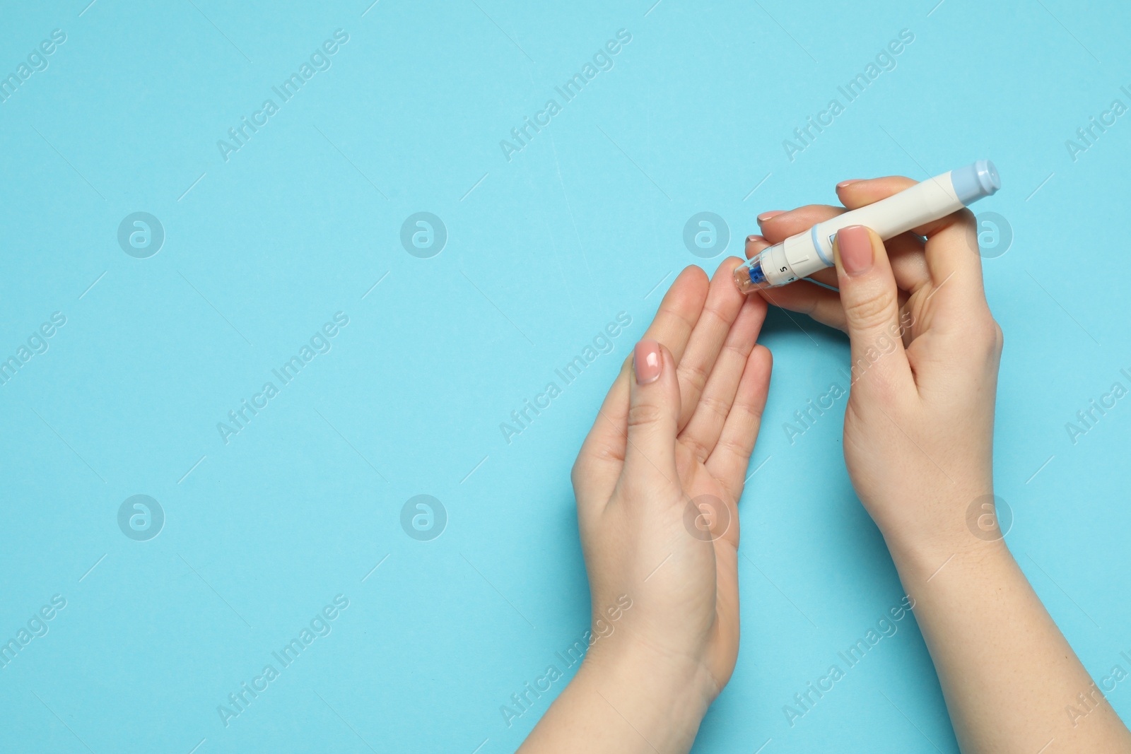 Photo of Diabetes. glucose testing. Woman using lancet pen on blue background, top view. Space for text