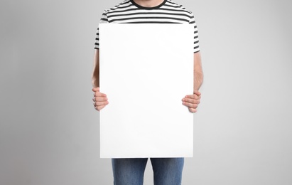 Photo of Man holding blank poster on light grey background, closeup