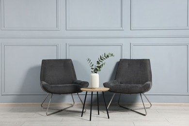 Photo of Comfortable armchairs, side table and eucalyptus indoors