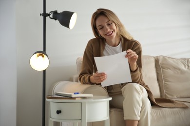 Happy woman reading letter on sofa at home