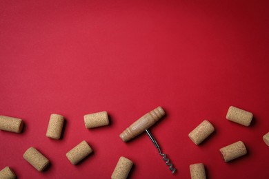 Photo of Corkscrew and wine bottle stoppers on red background, flat lay. Space for text