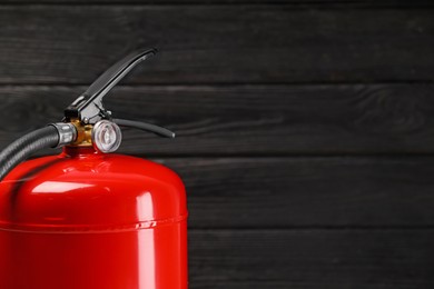 Photo of Fire extinguisher against wooden wall, closeup. Space for text