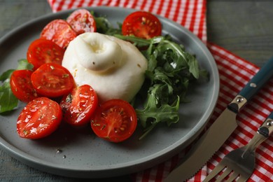 Delicious burrata cheese with tomatoes and arugula served on grey wooden table, closeup