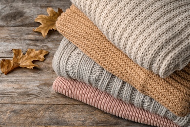 Photo of Stack of folded knitted sweaters and autumn leaves on table, closeup. Space for text