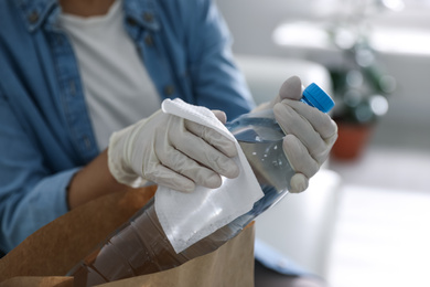 Woman cleaning bottle of water with wet wipe indoors, closeup