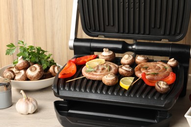 Photo of Electric grill with homemade sausages, vegetables and spices on wooden table