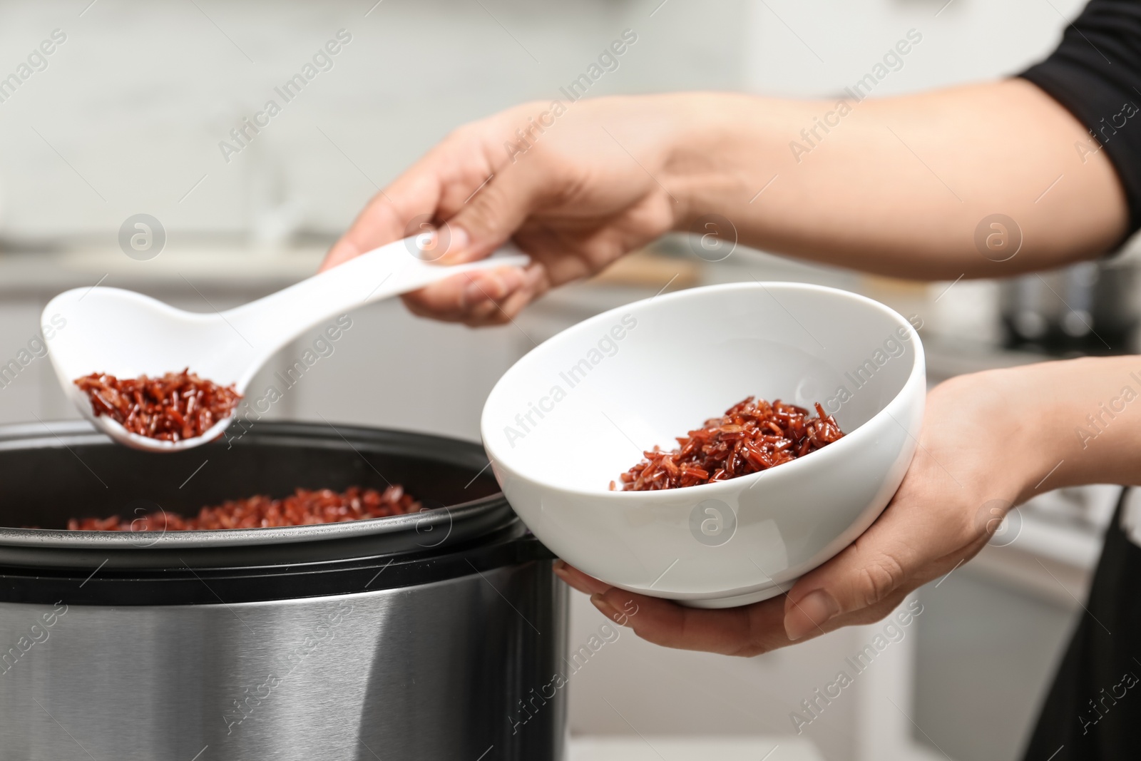 Photo of Woman putting brown rice into bowl from multi cooker in kitchen, closeup