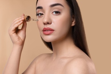 Photo of Young woman applying essential oil onto face on beige background
