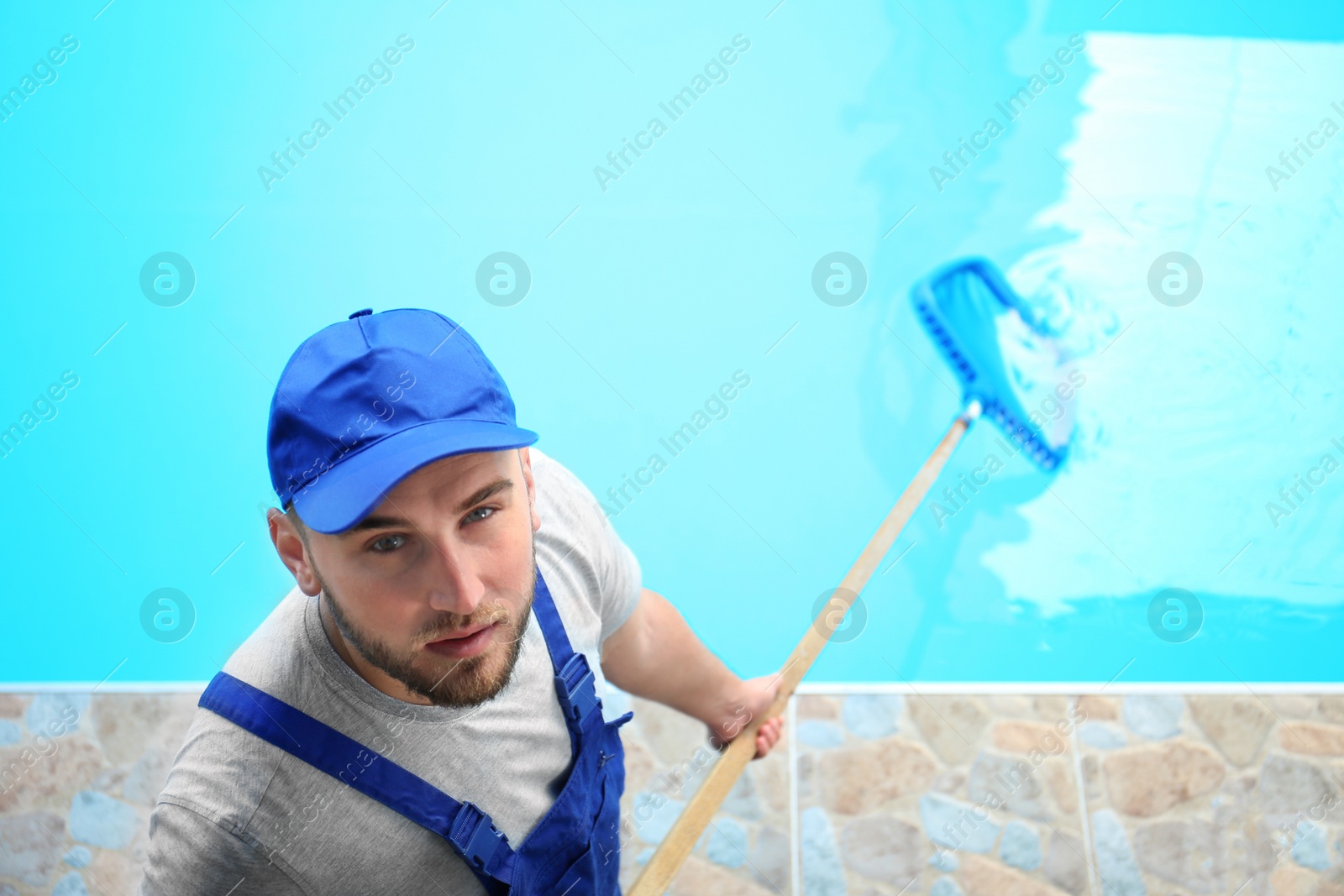 Photo of Male worker cleaning outdoor pool with scoop net