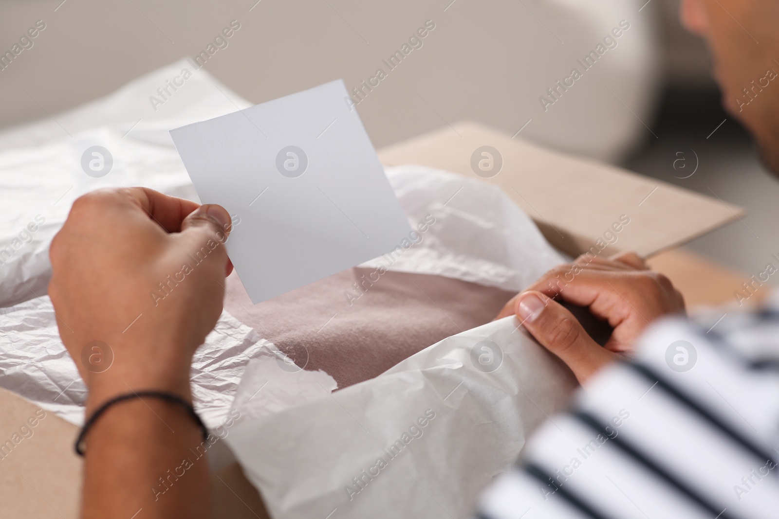 Photo of Young man holding greeting card near parcel with Christmas gift, closeup