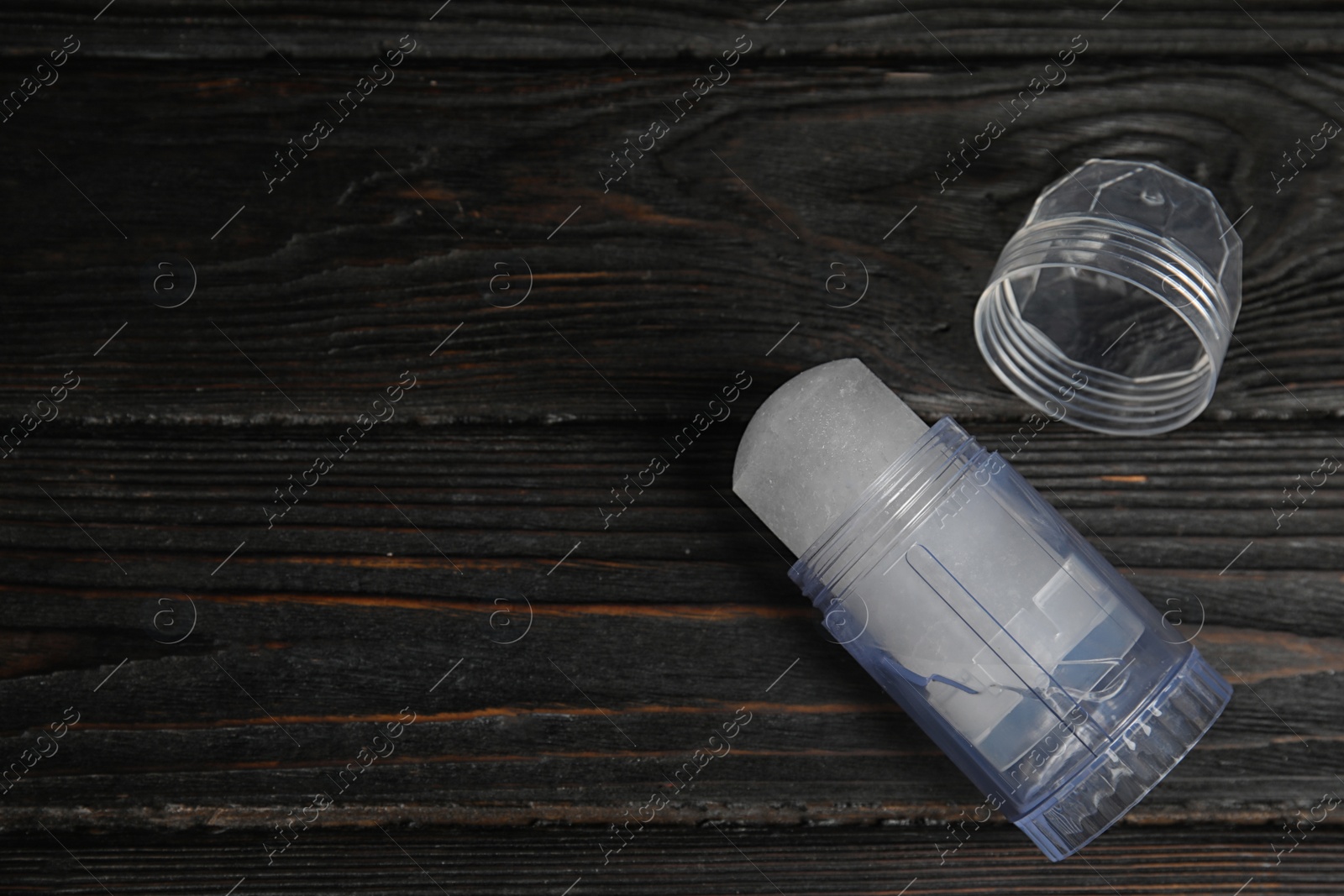 Photo of Natural crystal alum deodorant and cap on black wooden table, above view. Space for text