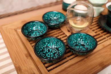 Photo of Wooden tray with cups for traditional tea ceremony on pink fabric, closeup