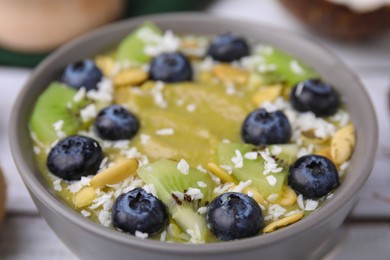 Photo of Bowl of delicious fruit smoothie with fresh blueberries, kiwi slices and coconut flakes on white wooden table, closeup