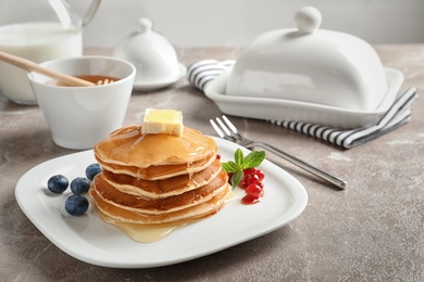 Photo of Stack of tasty pancakes with berries, butter and honey on table