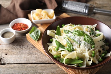 Photo of Delicious pasta with green peas, fresh basil and cheese on wooden table, closeup