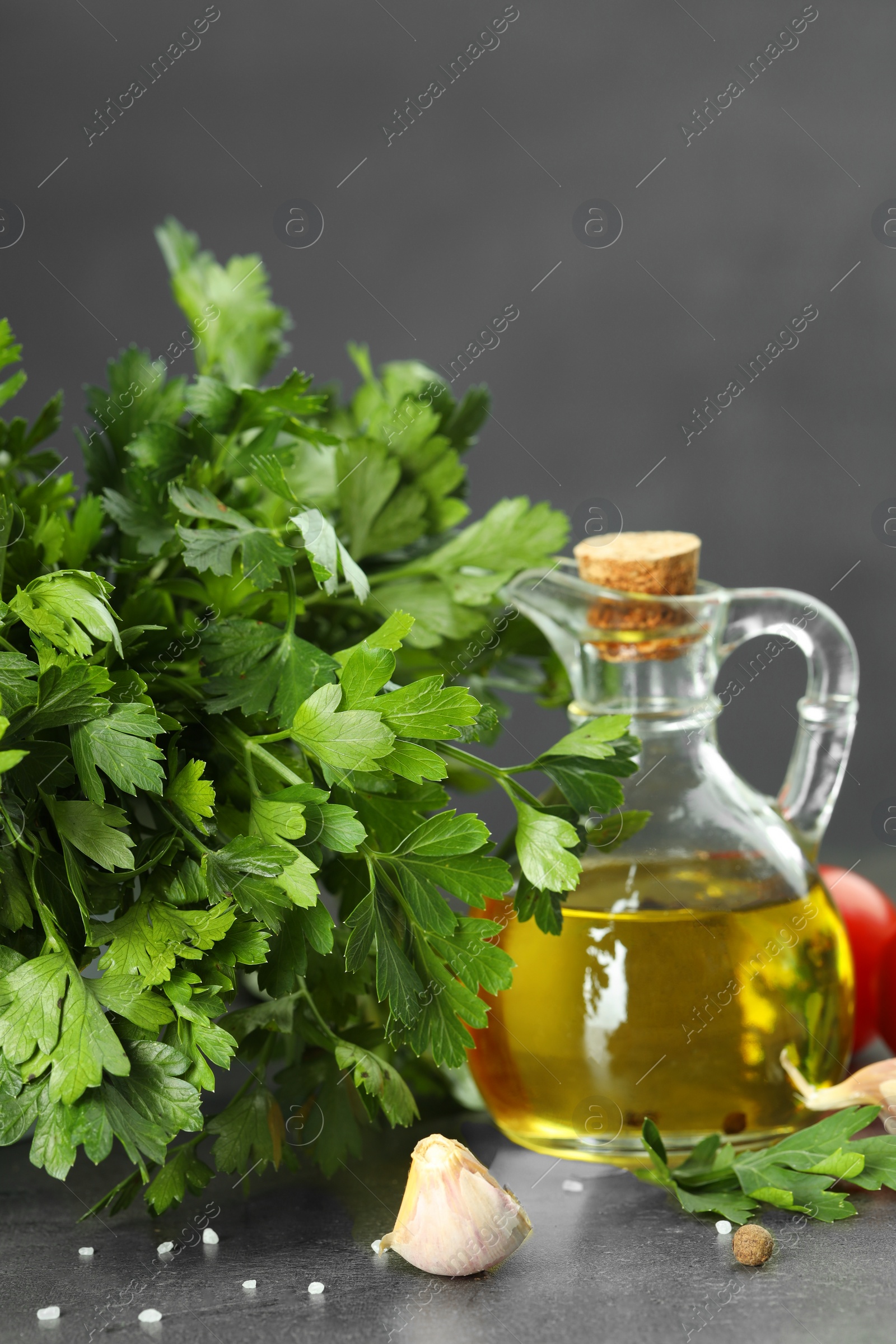 Photo of Fresh parsley, oil and other products on grey table, closeup