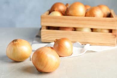 Photo of Ripe onions and wooden crate on light table against blue background, space for text