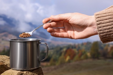 Photo of Woman pouring instant coffee into cup in mountains, closeup