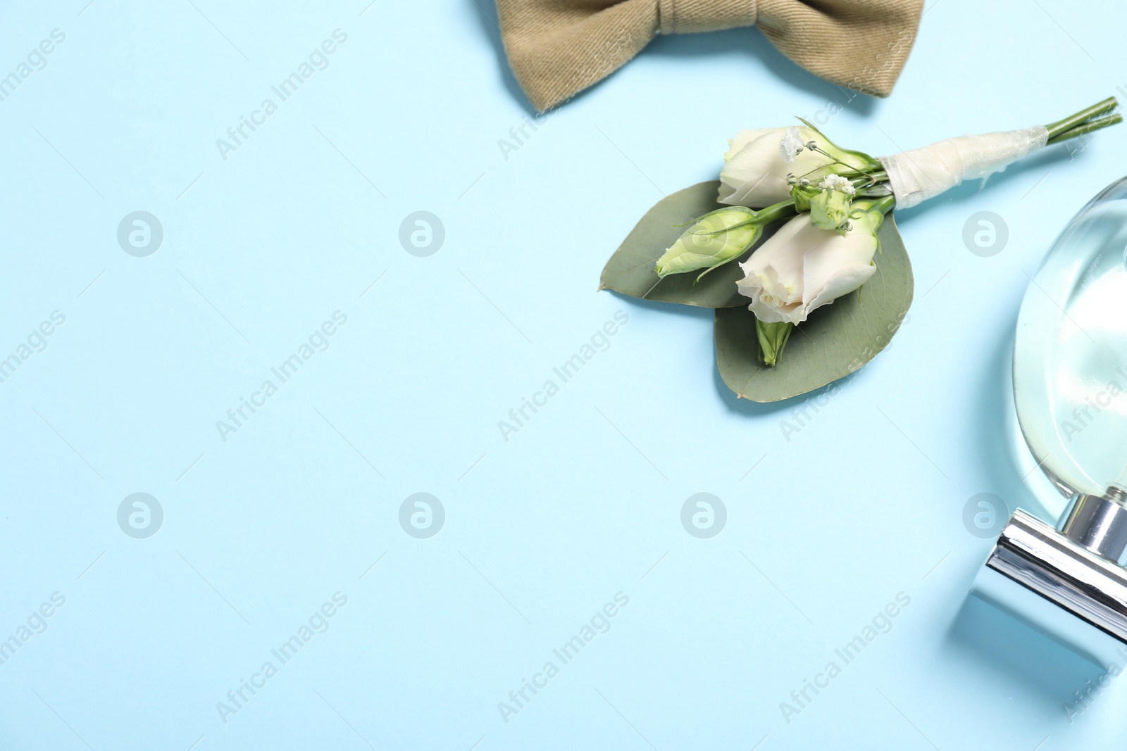 Photo of Wedding stuff. Stylish boutonniere, bow tie and perfume on light blue background, space for text