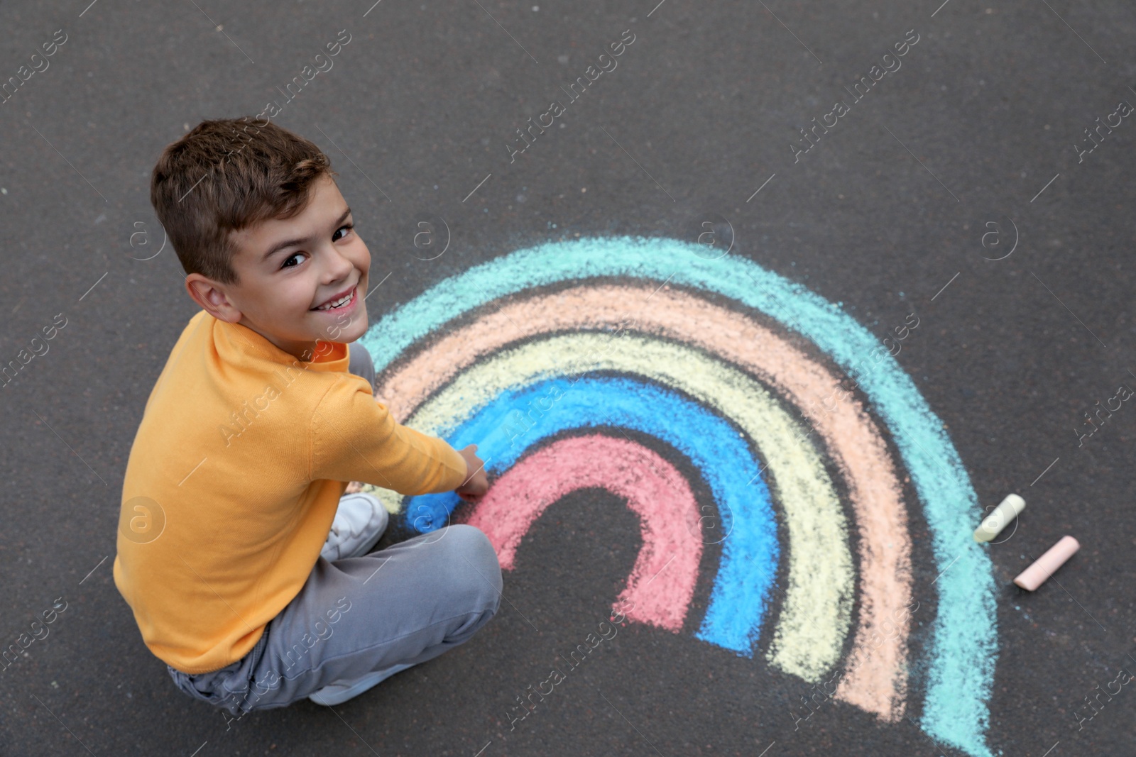 Photo of Happy child drawing rainbow with chalk on asphalt, above view