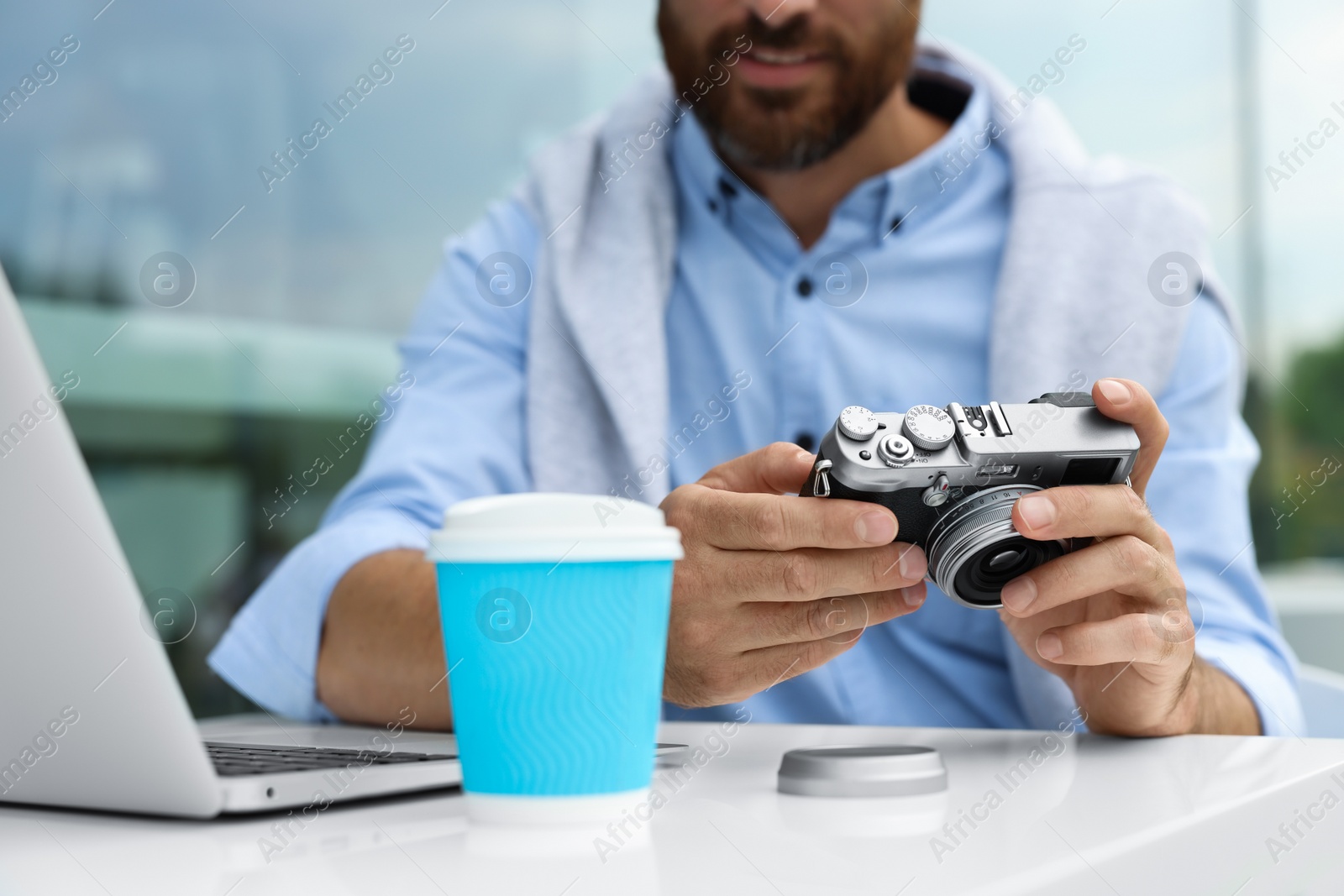 Photo of Man with camera, coffee and laptop in outdoor cafe, closeup. Interesting hobby