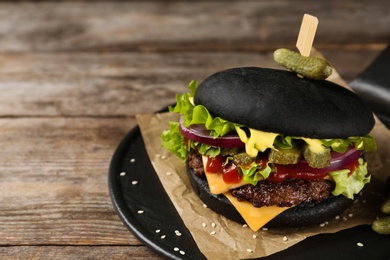 Photo of Slate plate with black burger on table, closeup. Space for text