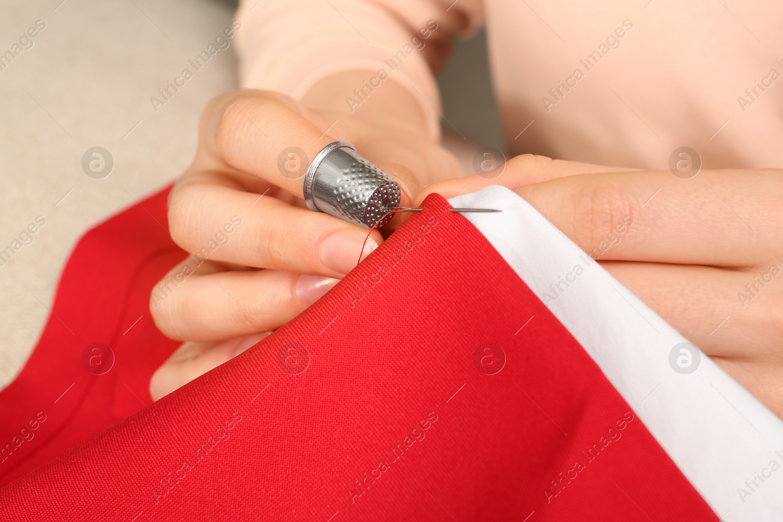 Photo of Woman sewing on red fabric with thimble and needle, closeup