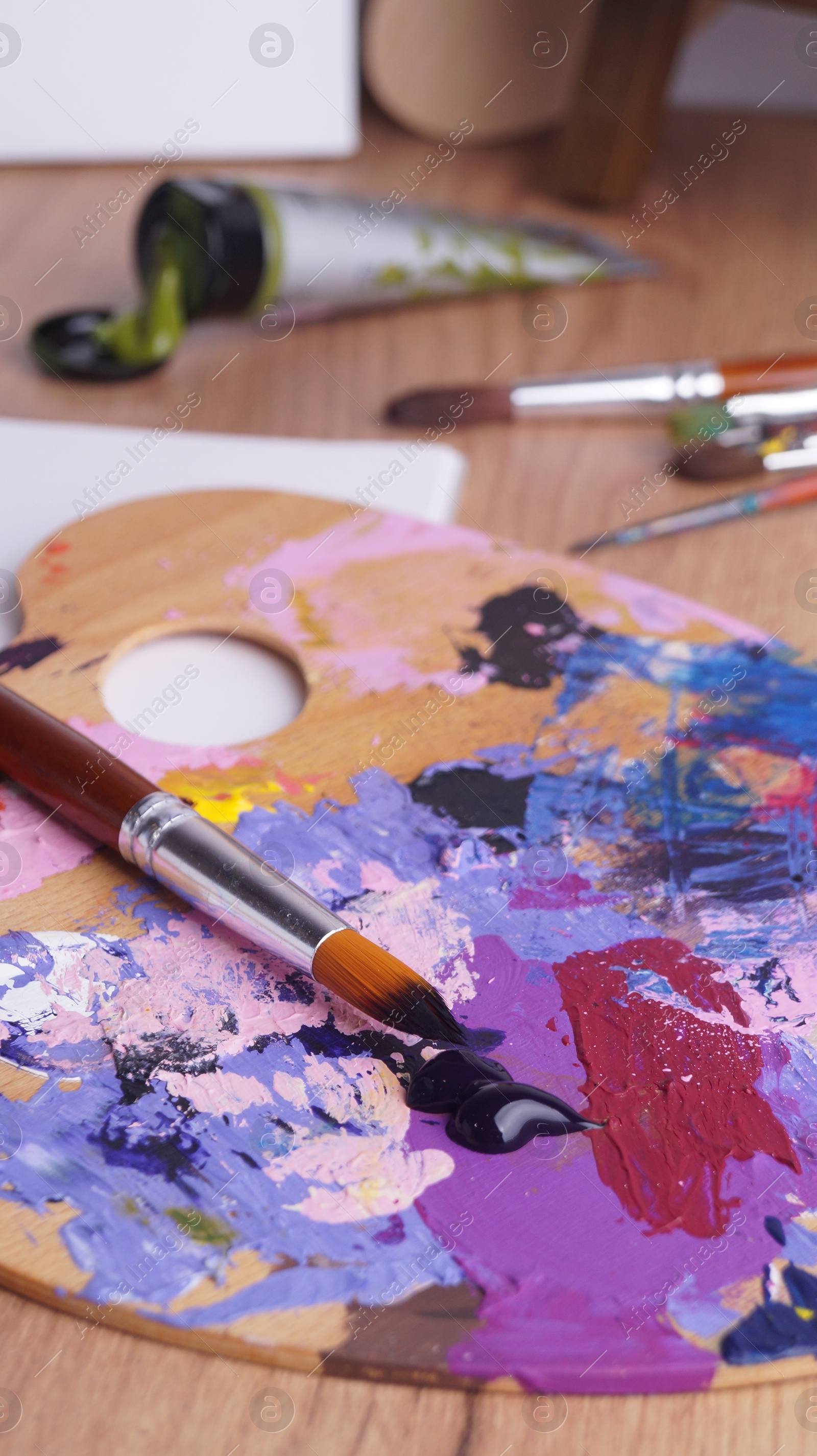 Photo of Artist's palette with mixed paints and brushes on wooden table