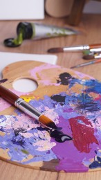 Artist's palette with mixed paints and brushes on wooden table