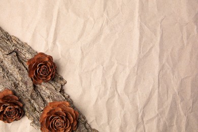 Photo of Tree bark piece and cones on beige crumpled paper, top view. Space for text