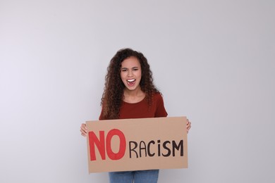Emotional African American woman holding sign with phrase No Racism on light background