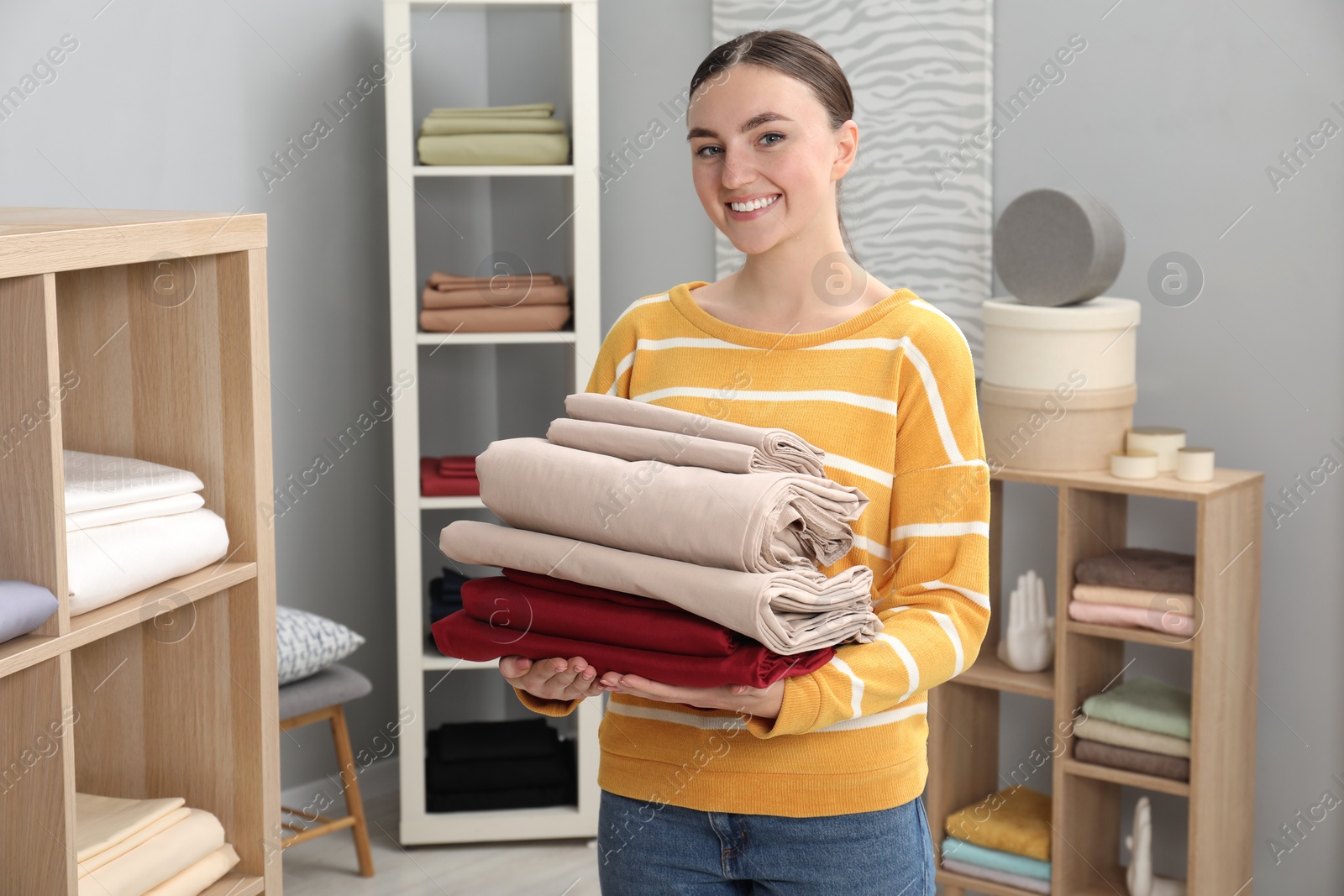 Photo of Smiling young woman with stack of bed linens in shop