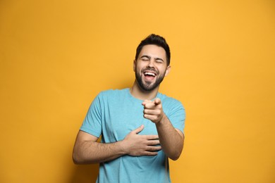 Young man laughing on yellow background. Funny joke