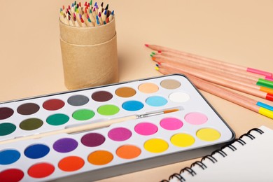 Watercolor palette with brush and colorful pencils on beige background