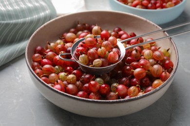 Bowl and sieve with ripe gooseberries on light grey marble table