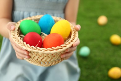 Photo of Cute little girl with basket full of Easter eggs outdoors, closeup