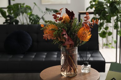 Photo of Vase with bouquet of beautiful leucospermum flowers and air freshener on side table in room, space for text