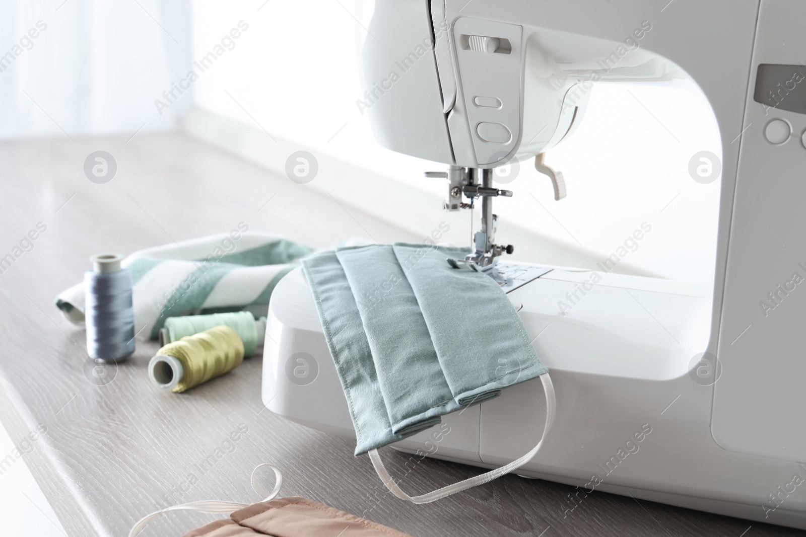 Photo of Sewing machine with homemade protective mask and threads on wooden table