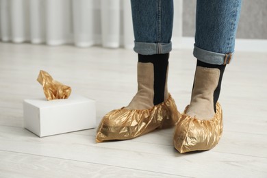 Photo of Woman wearing shoe covers onto her boots indoors, closeup