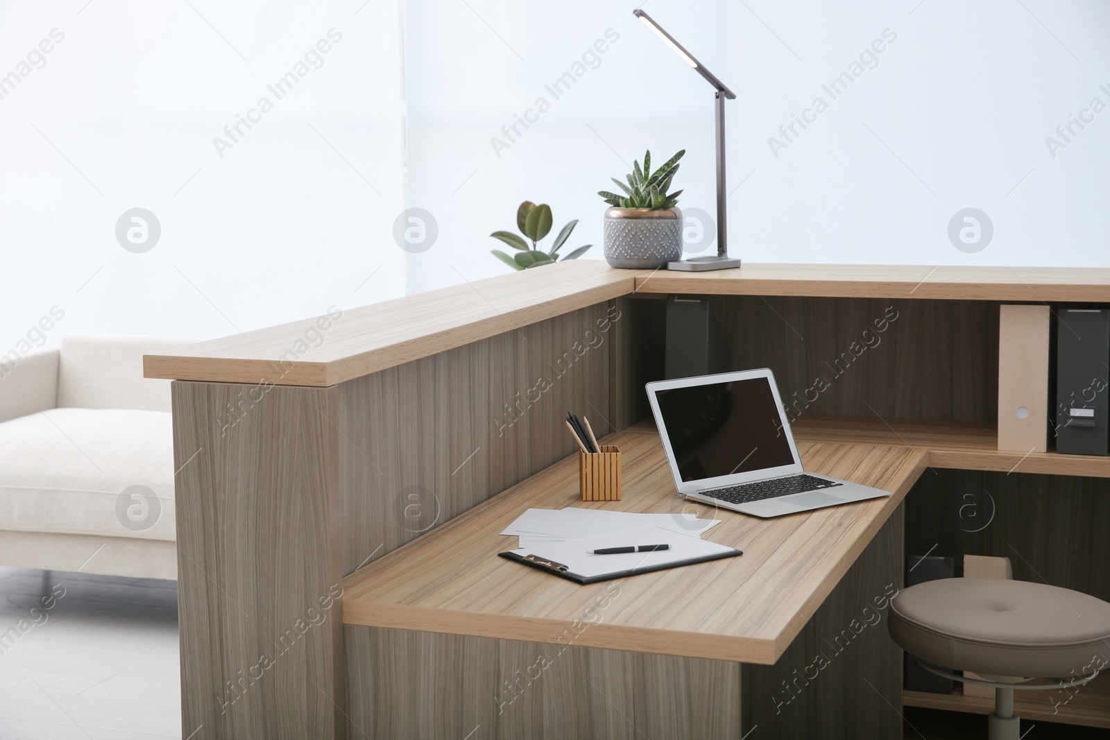 Photo of Stylish modern wooden desk with laptop indoors. Receptionist workplace