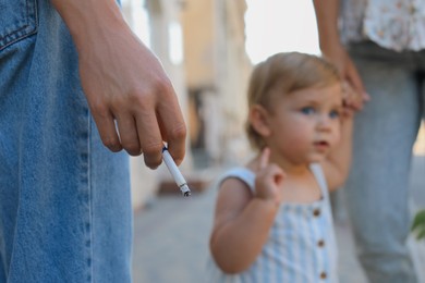 Photo of Woman smoking cigarette in public place outdoors, closeup. Don't smoke near kids