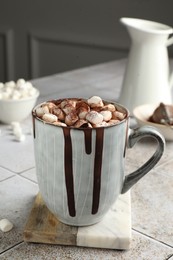 Photo of Delicious hot chocolate with marshmallows and cocoa powder in cup on tiled table