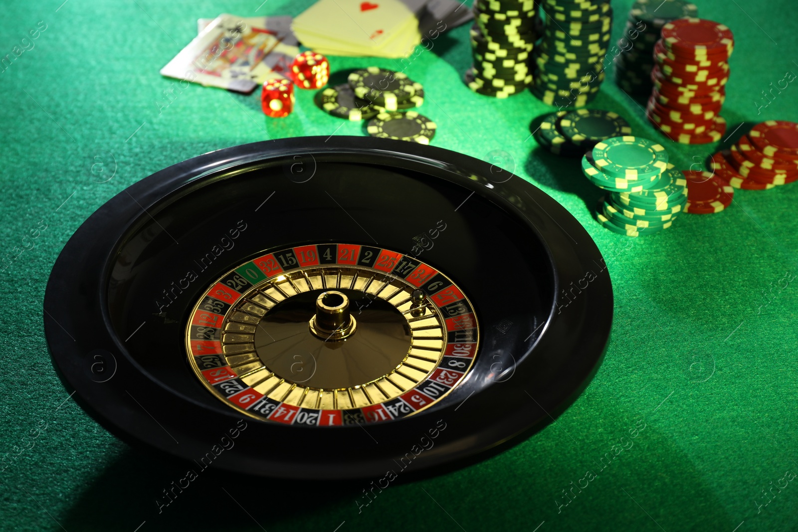 Photo of Roulette wheel with ball, playing cards and chips on green table. Casino game