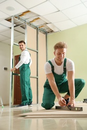 Photo of Young workers installing drywall indoors. Home repair service